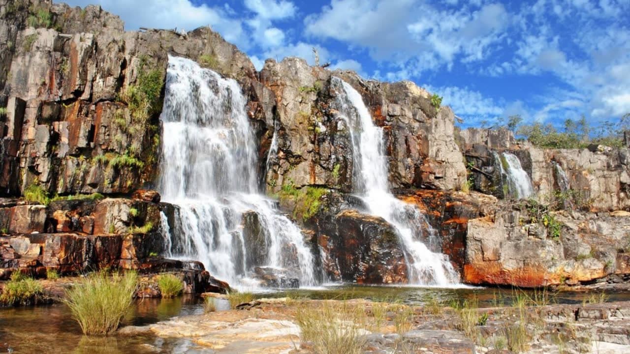 Cachoeira larga despencando por paredão avermelhado em dois braços paralelos